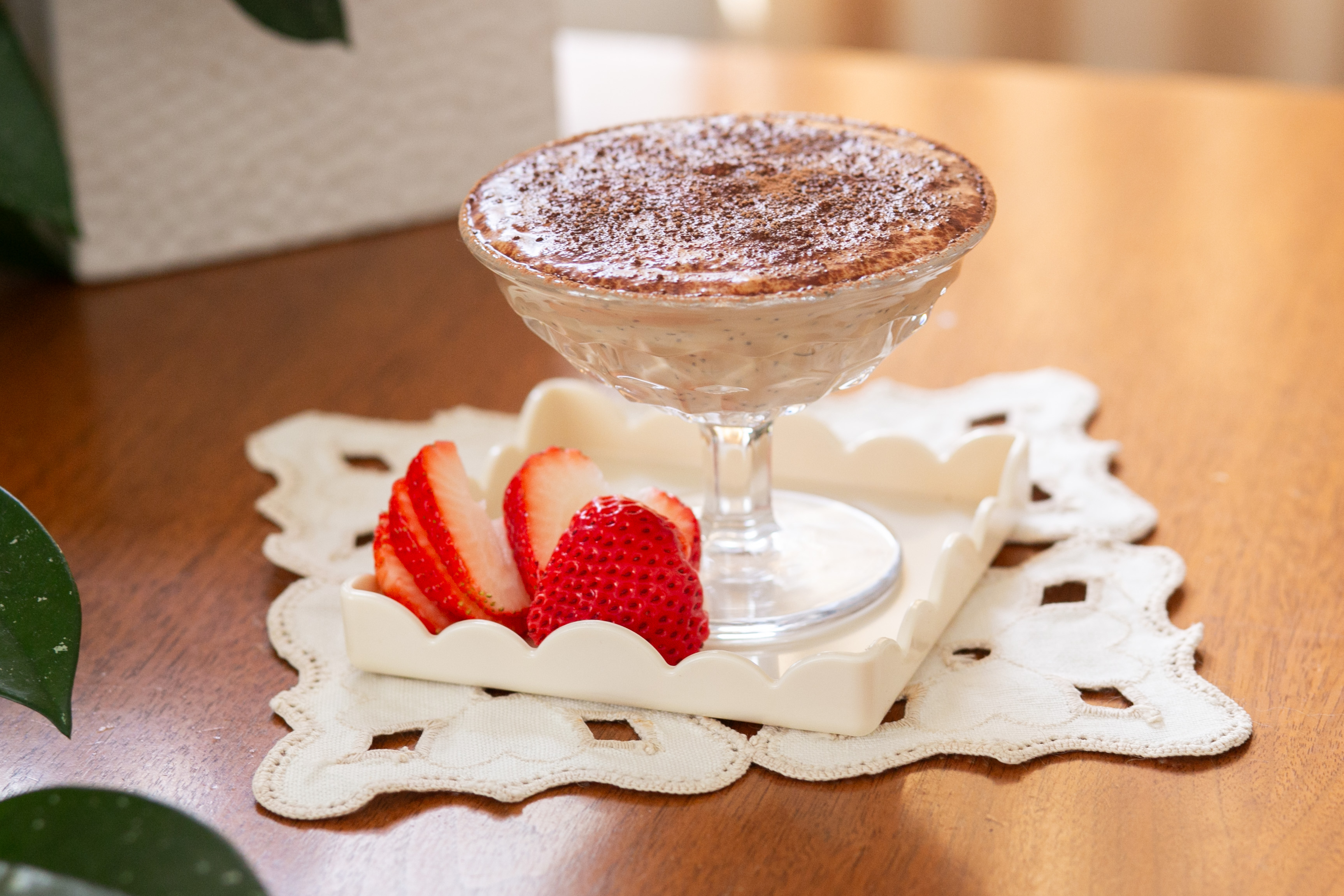 Tiramisu chia pudding dusted with cocoa powder in a footed glass dish, served with sliced strawberries on a white plate