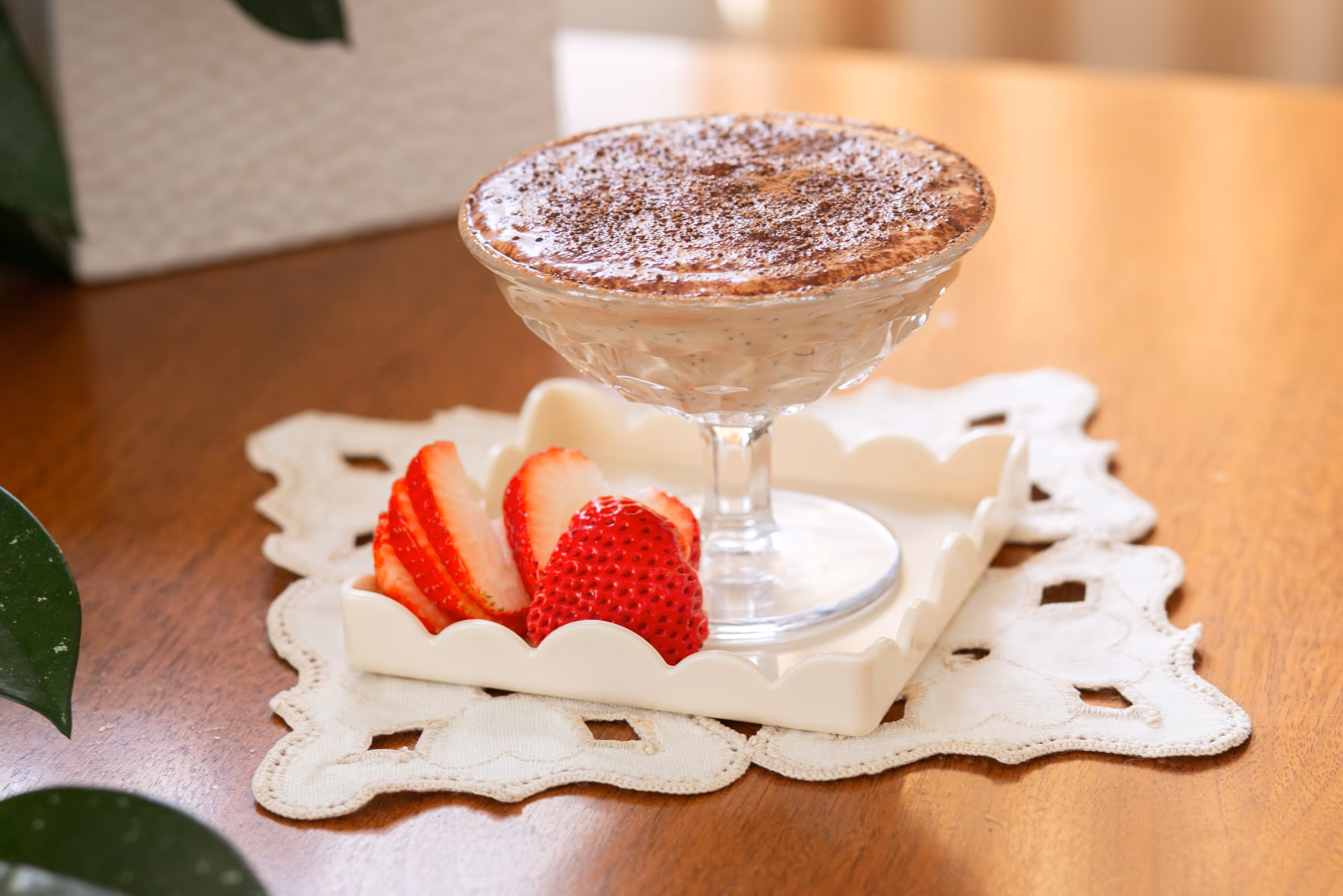 Tiramisu chia pudding dusted with cocoa powder in a footed glass dish, served with sliced strawberries on a white plate