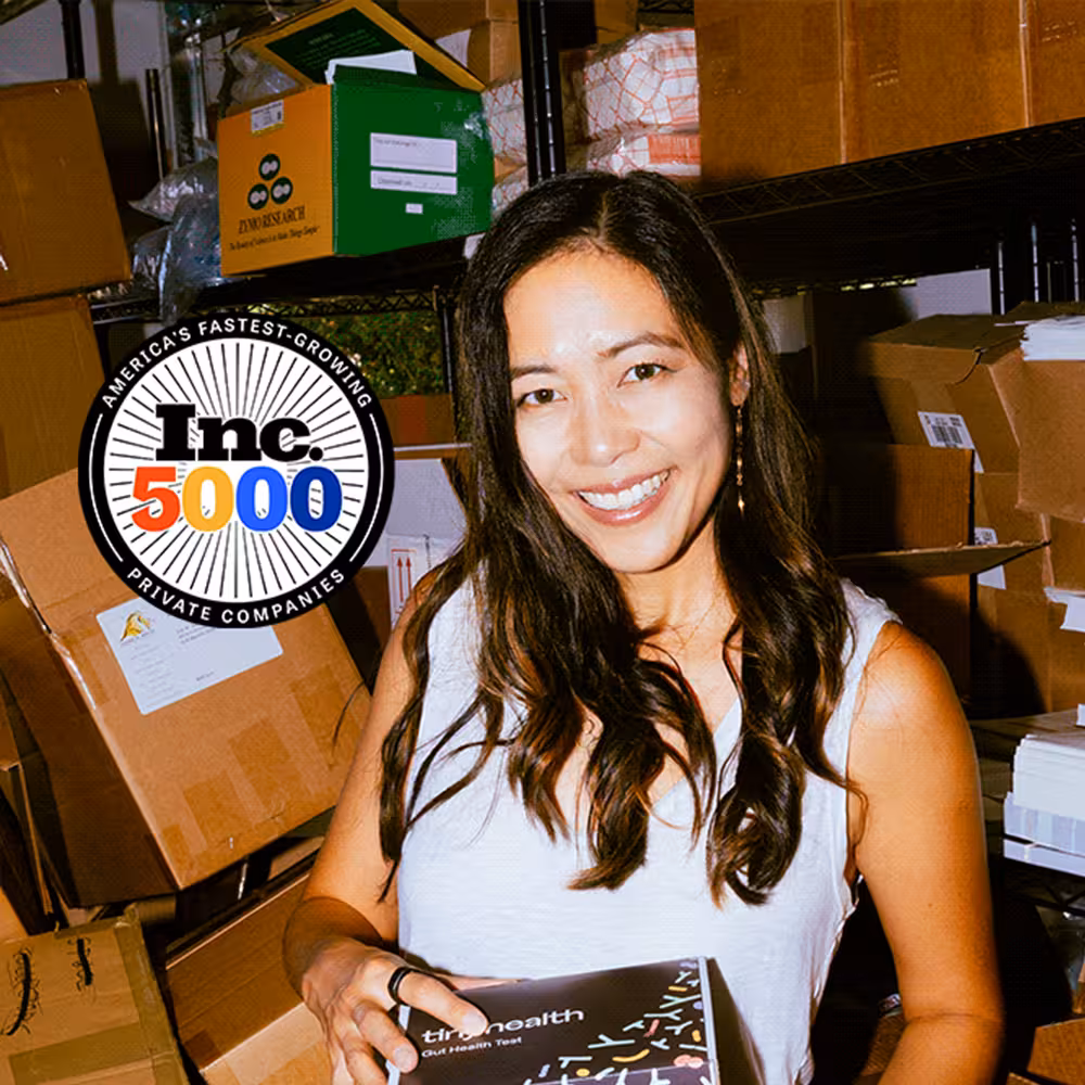 Cheryl Sew Hoy, Tiny Health co-founder, smiling with a Gut Health Test box in her garage, Inc. 5000 badge overlaid.