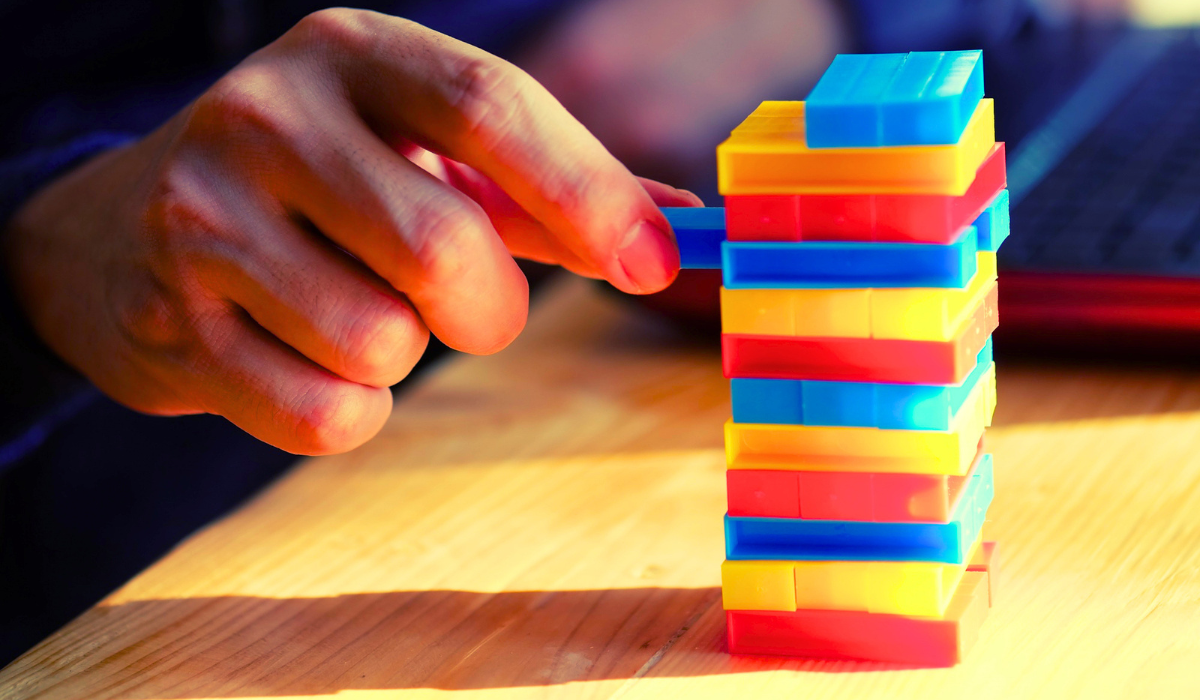 Mano che rimuove un blocco da una torre colorata in equilibrio, simbolo di strategia e valorizzazione dei talenti aziendali