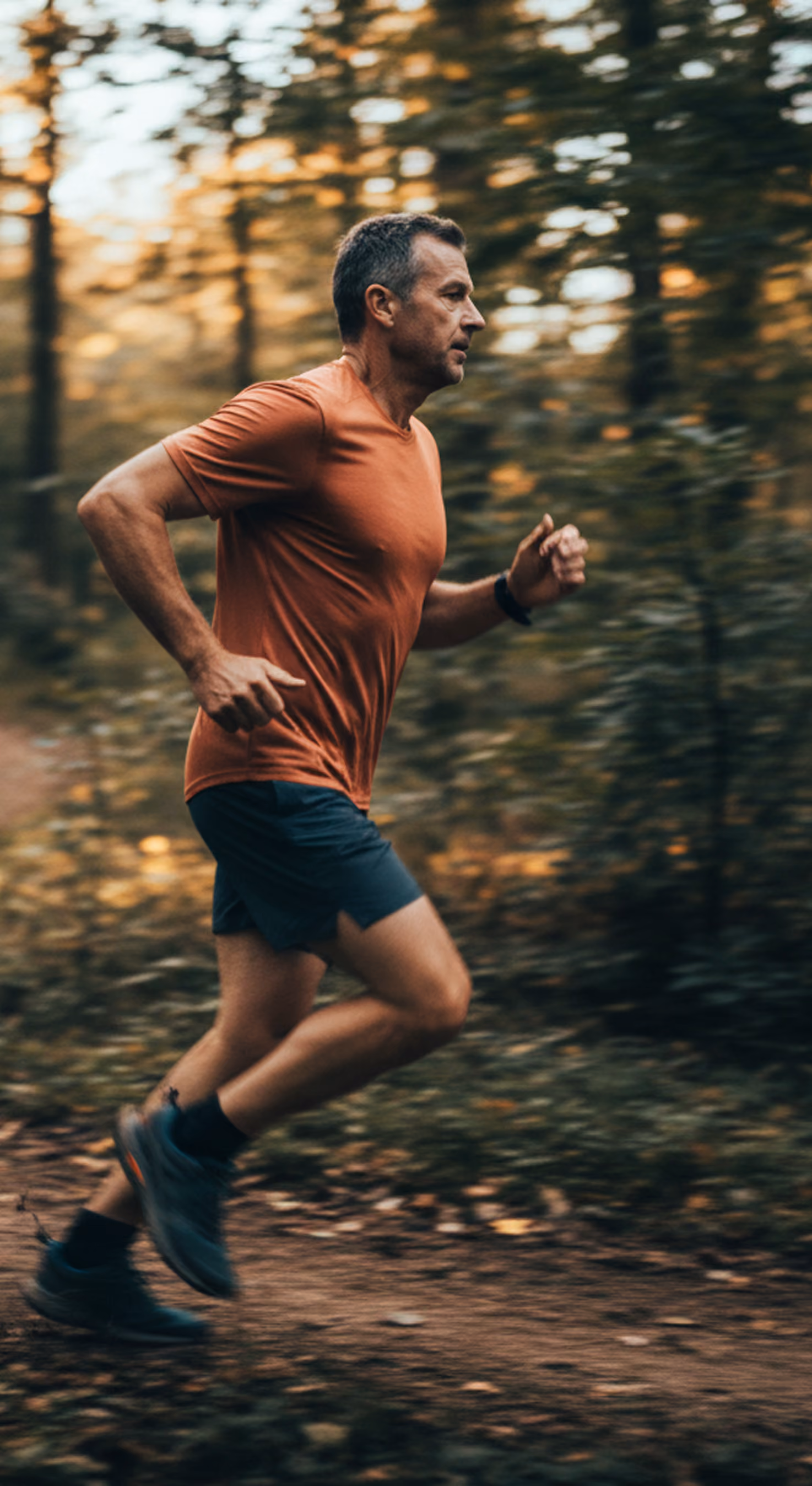 Man in an orange shirt running on a forest trail during daytime.