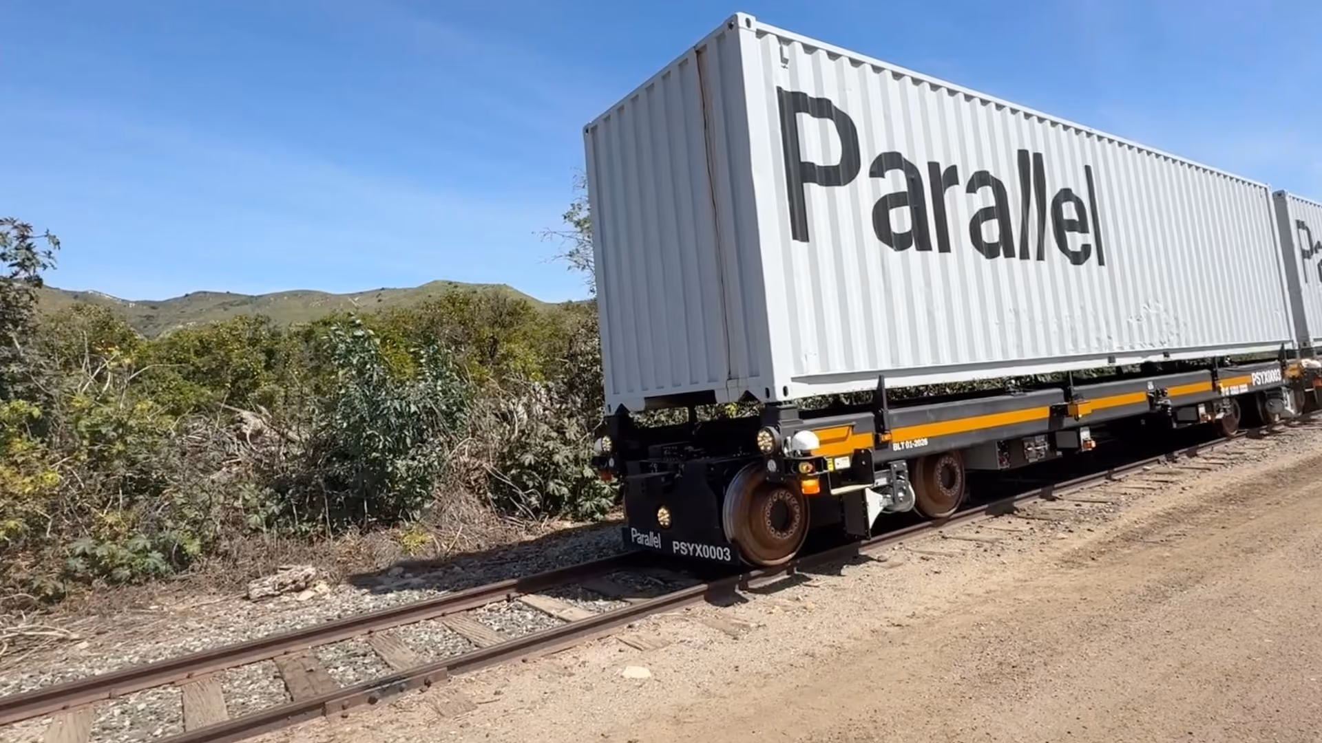 An autonomous rail container car branded "Parallel" standing on train tracks in open countryside.