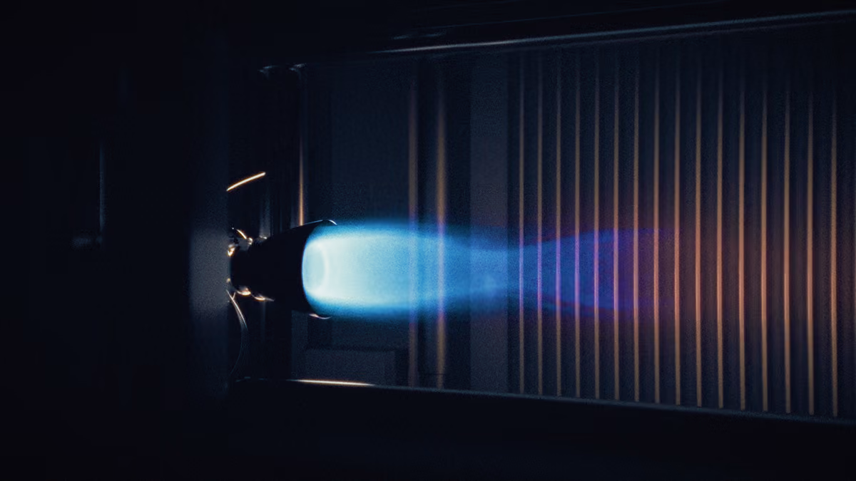 A rocket engine hot-fire test producing a bright blue-and-orange exhaust plume inside a test chamber.
