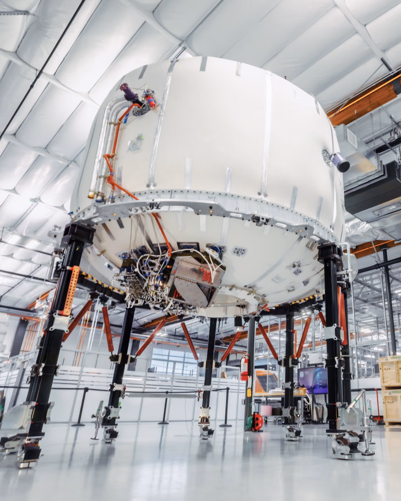 A large satellite under assembly on a support fixture inside a hangar.