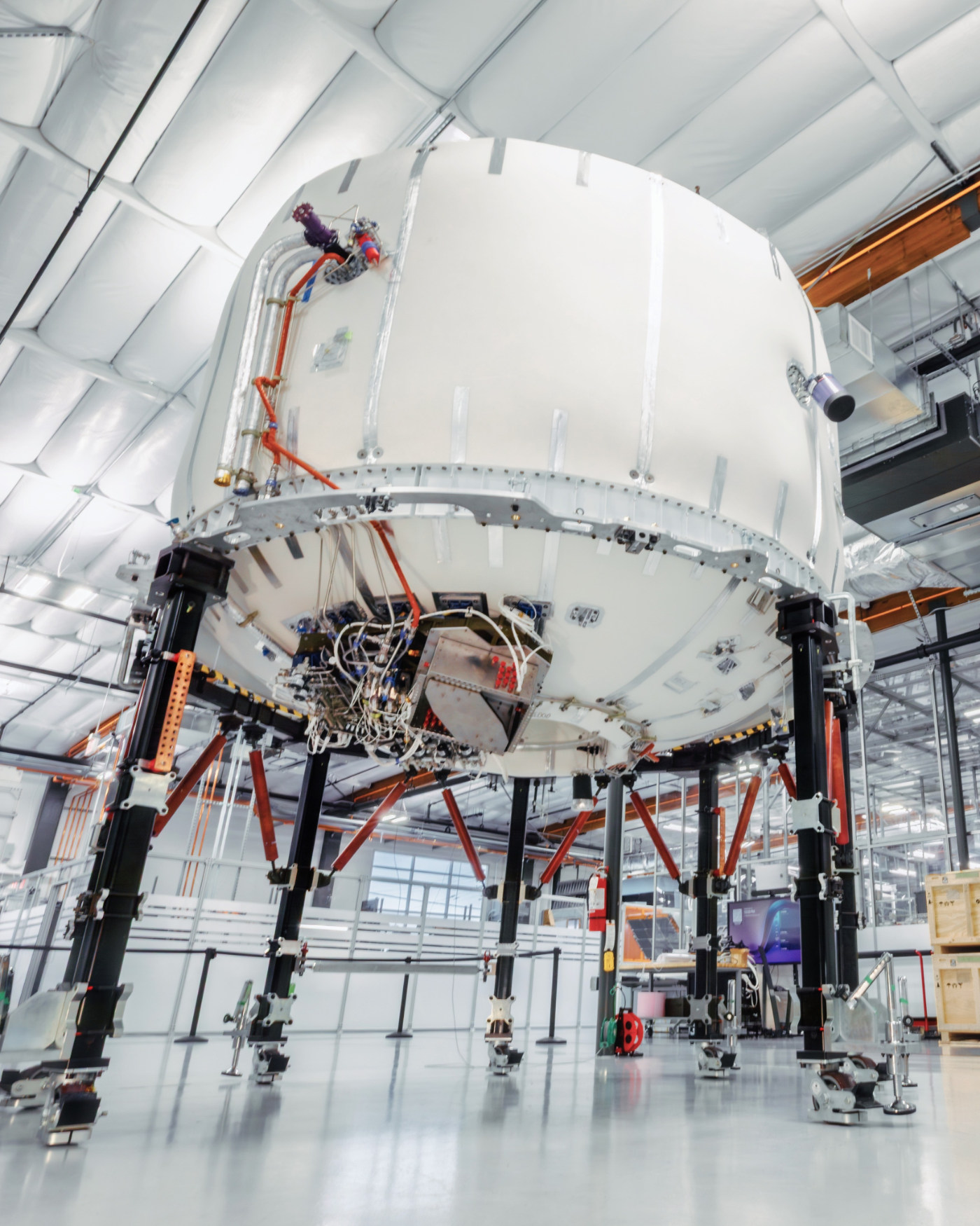 A large satellite under assembly on a support fixture inside a hangar.