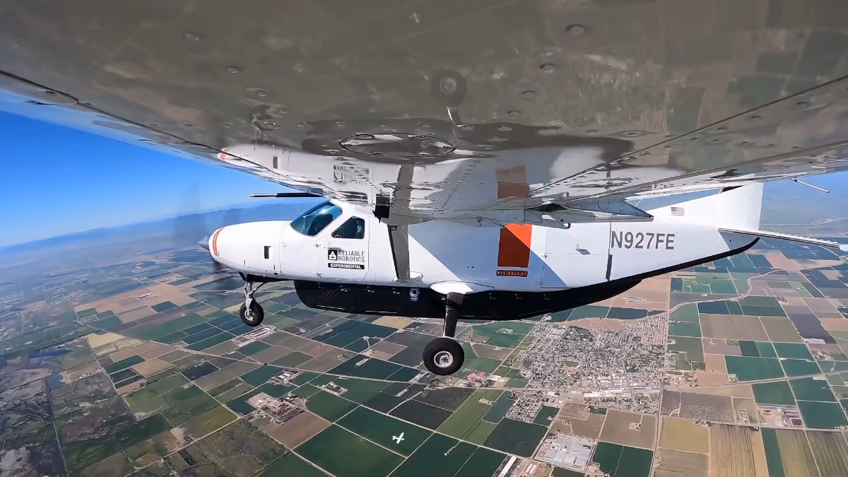A white single-engine aircraft flying above patchwork farmland.