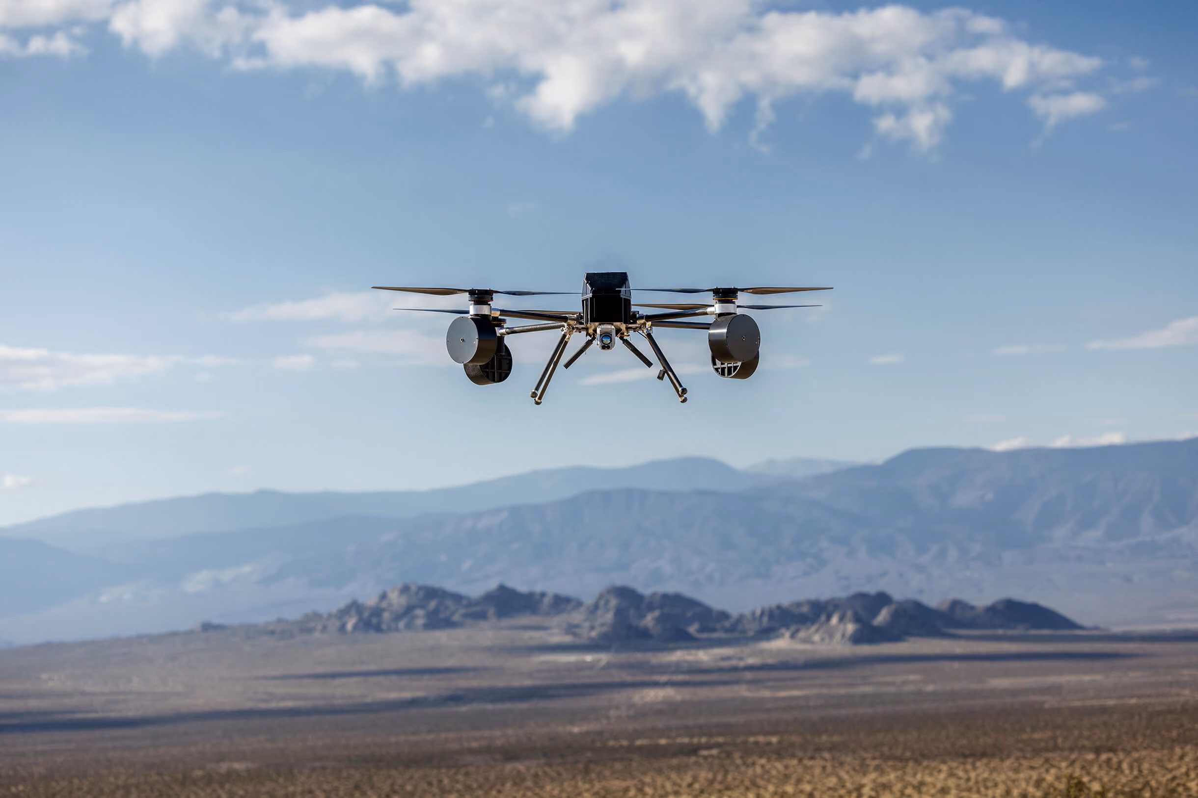 An uncrewed aircraft in flight above a desert mountain range.