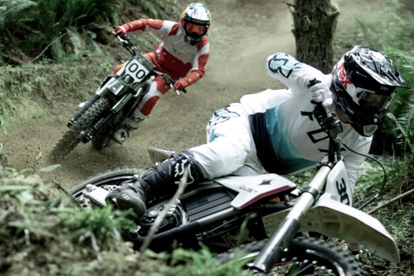 Two riders cornering Dust electric dirt bikes on a forest trail