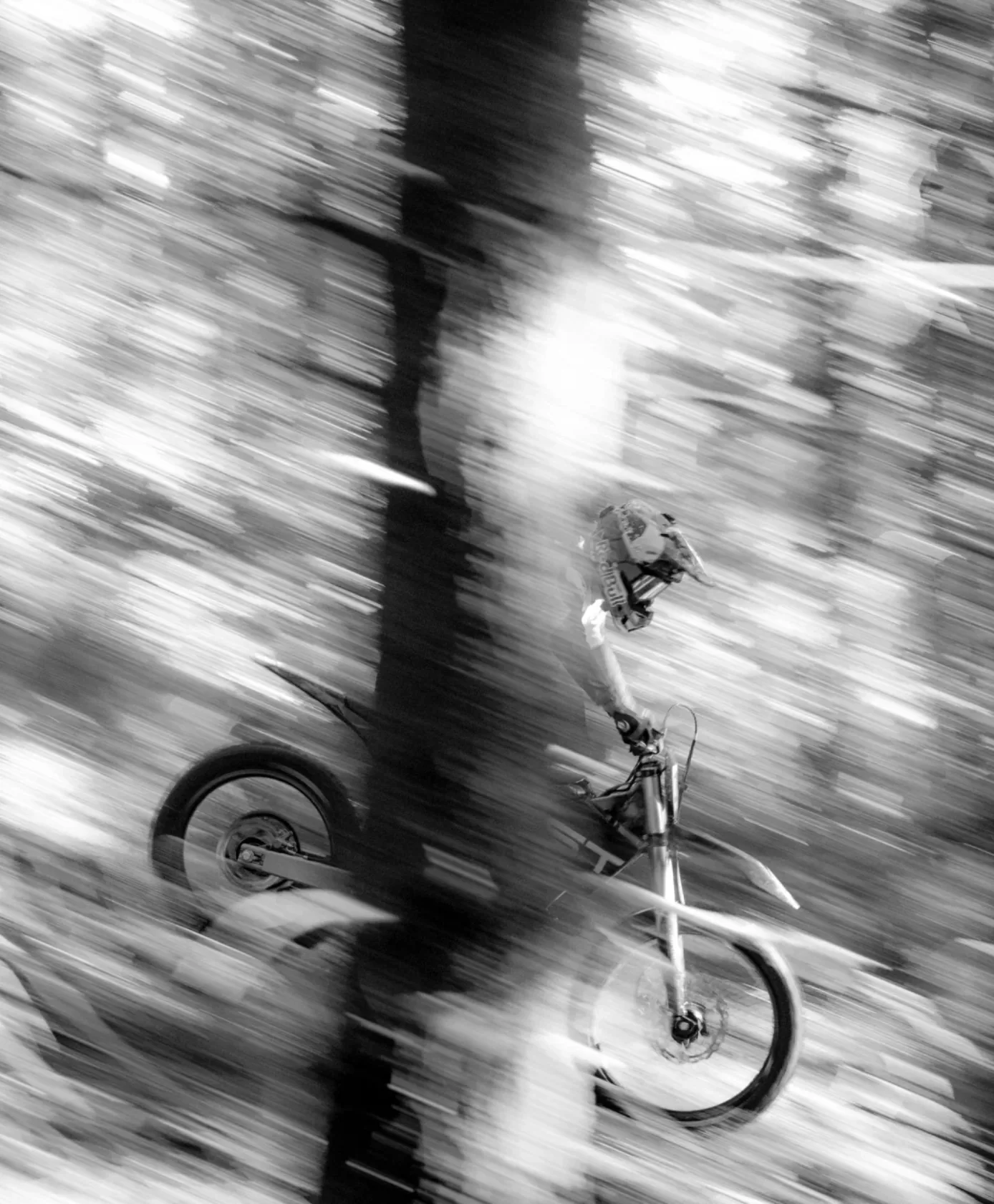 Black-and-white, motion-blurred photo of a rider on a Dust Moto dirt bike in the forest