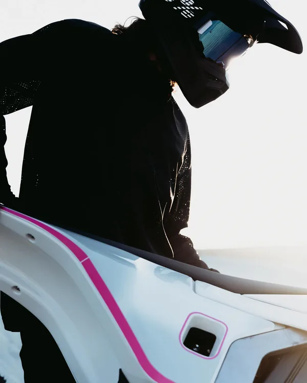 A Dust Moto rider in helmet and goggles leaning over the white bodywork of an electric dirt bike.
