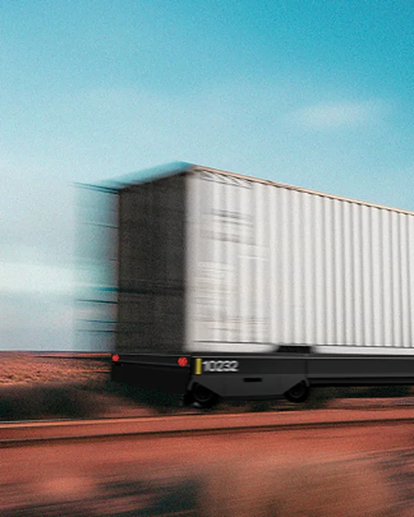 A Parallel rail car carrying a white shipping container, blurred with speed across open desert under a blue sky.