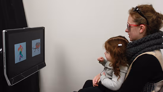 Woman and young girl sitting and looking at two colorful images displayed on a computer screen.