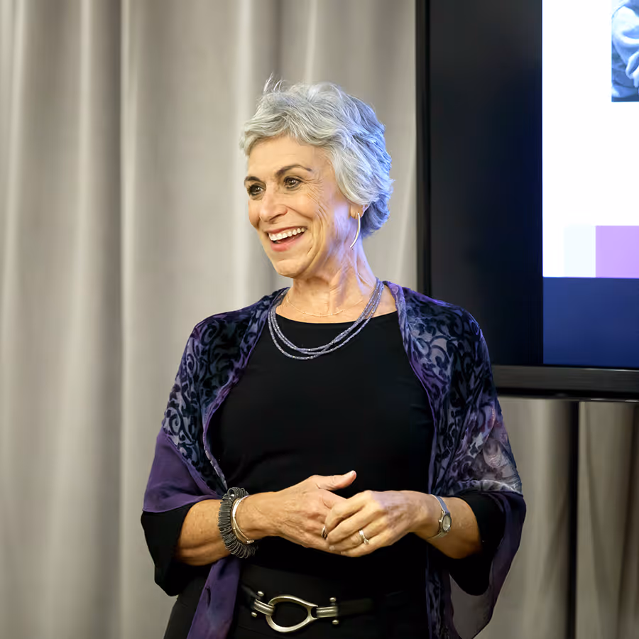 Smiling elderly woman with short gray hair wearing a purple shawl and black top.