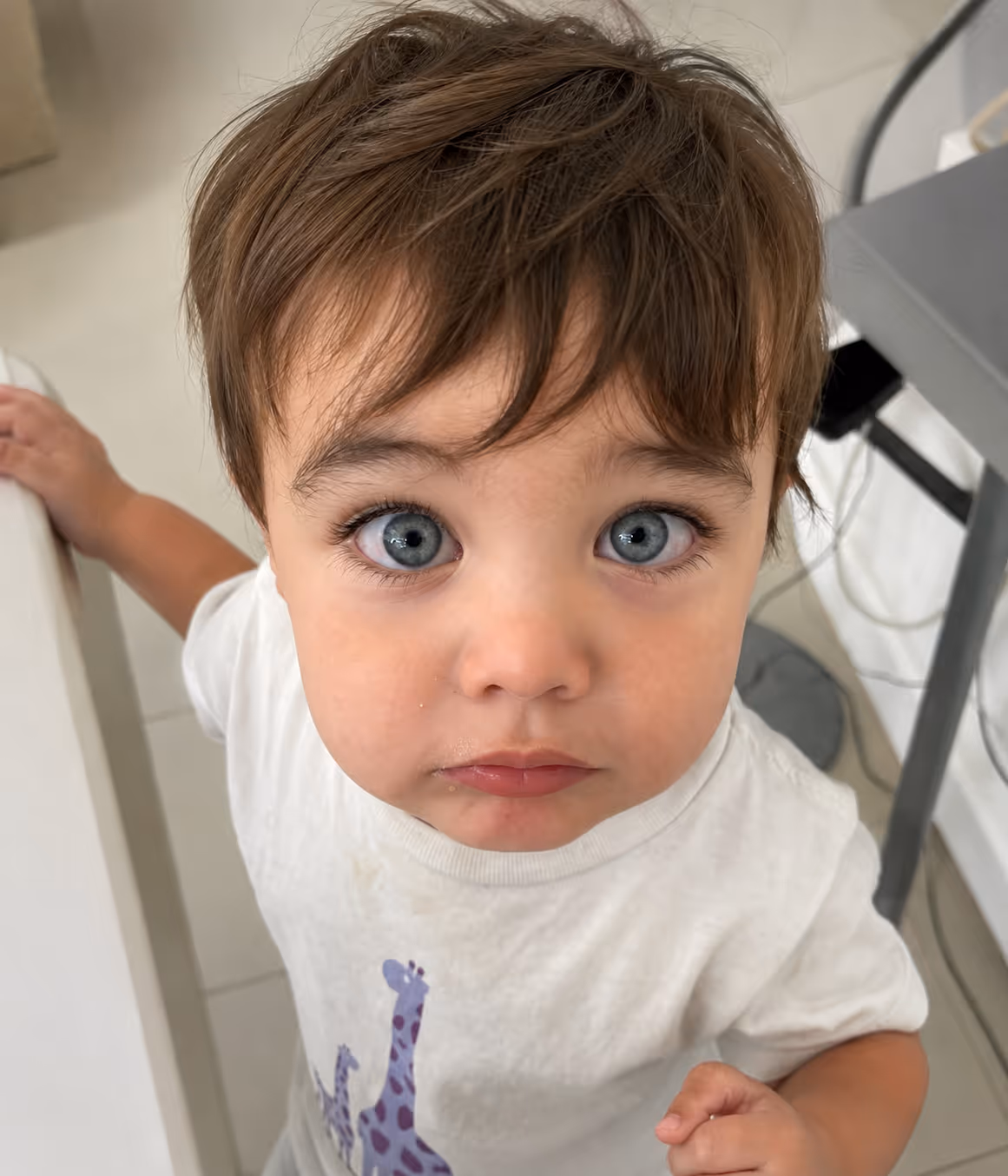 Close-up of a toddler with blue eyes and light brown hair wearing a white shirt with purple giraffes.