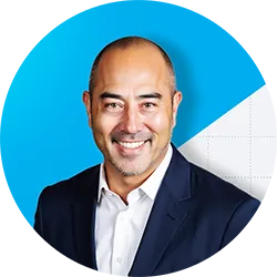 Smiling bald man wearing a dark suit jacket and white shirt with a blue and white background.