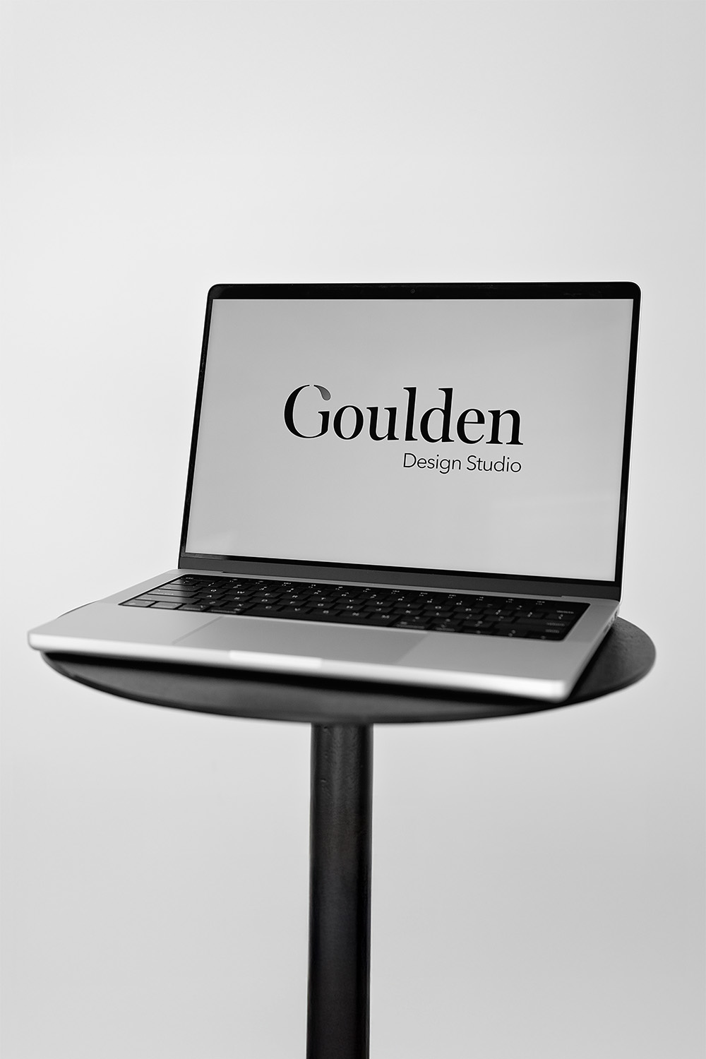Goulden Design Studio Logo displayed on a MacBook Pro placed on a stool