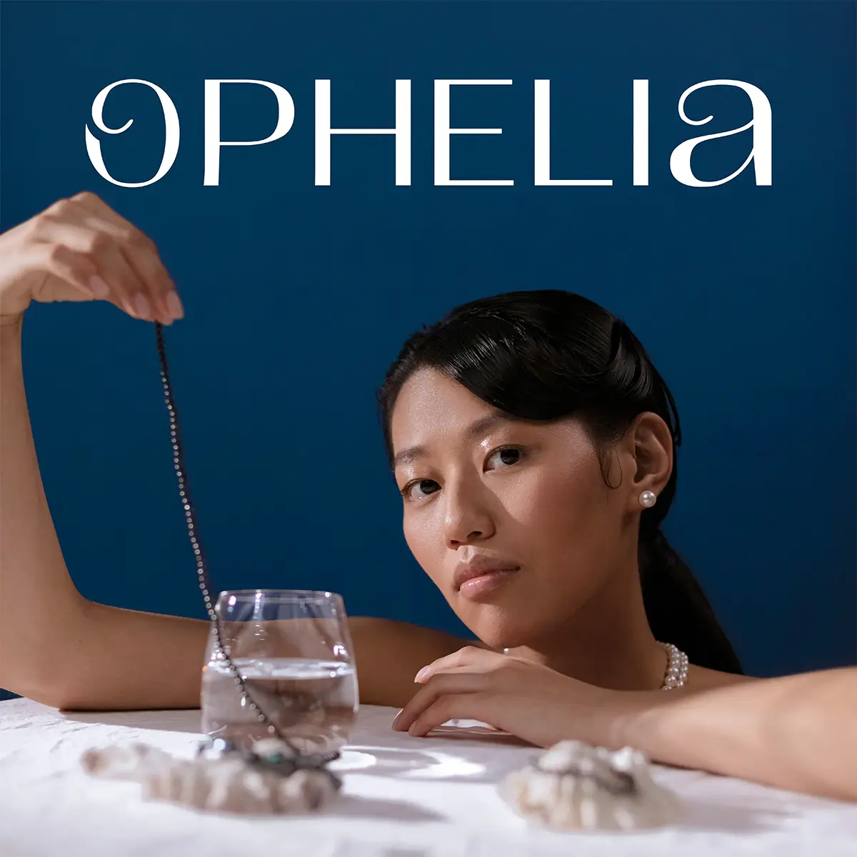 Ophelia brand and website design case study. Ophelia logo behind a luxurious women holding a necklace while leaning on a table top.