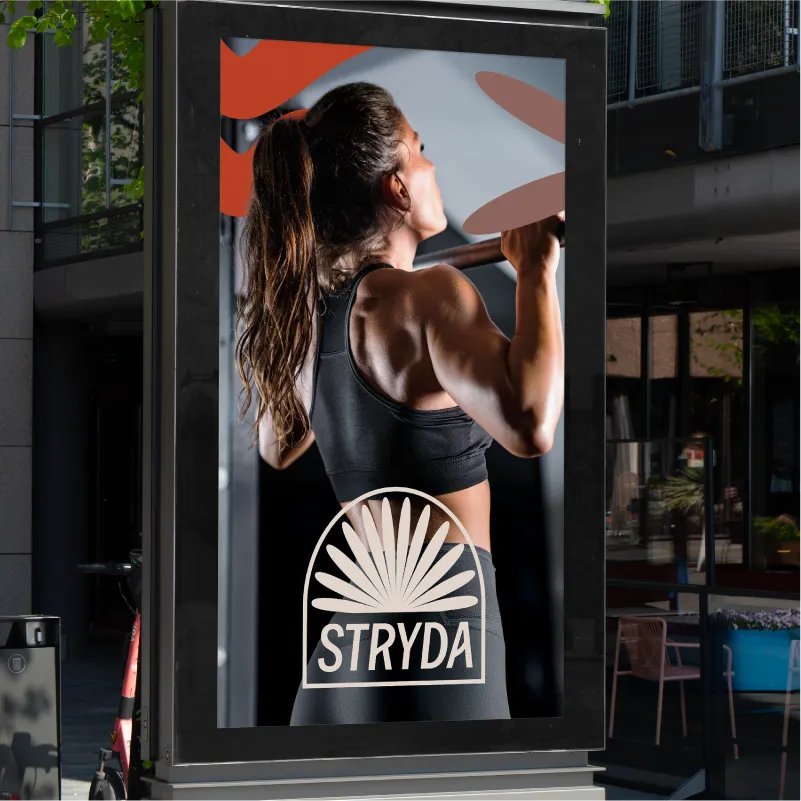 A digital poster design in the middle of a city centre featuring an athletic woman in black sportswear doing a pull-up in a gym with STRYDA logo overlay and abstract brand graphics.