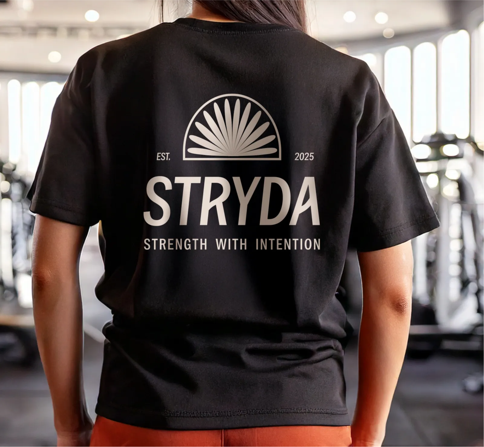 Person wearing a black T-shirt with the text 'EST. 2025 STRYDA Strength With Intention' and the STRYDA logo inspired by a New Zealand Falcon's tail graphic on the back.