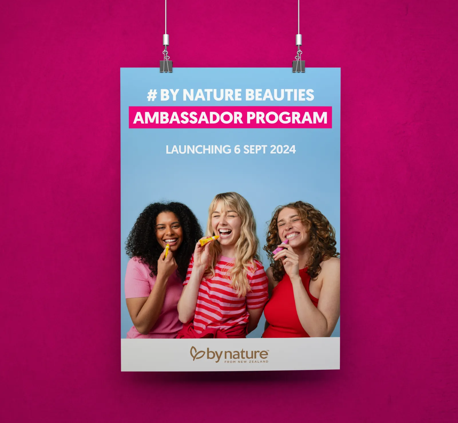 Poster announcing By Nature Beauties Ambassador Program launching 6 Sept 2024, featuring three smiling women holding colorful lip balm tubes against a blue background.