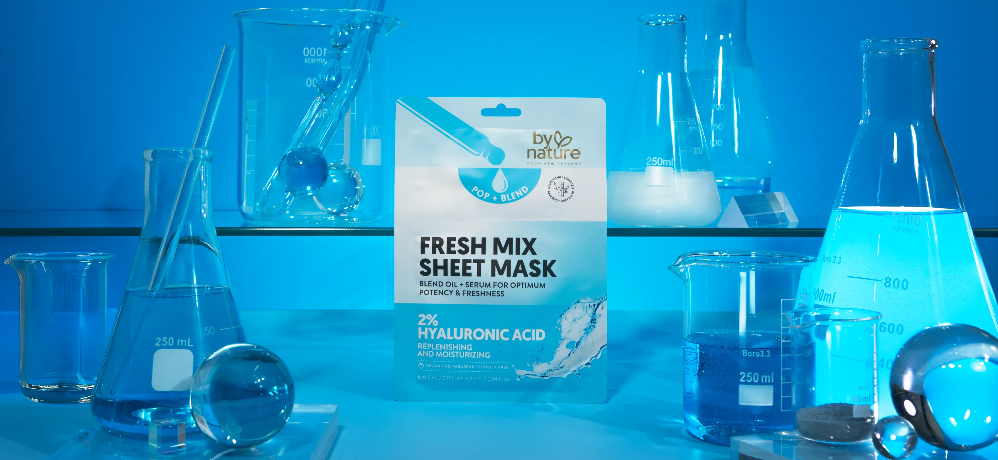 By Nature Fresh Mix Sheet Mask with 2% hyaluronic acid packaging surrounded by laboratory glassware with blue liquid on a blue background.