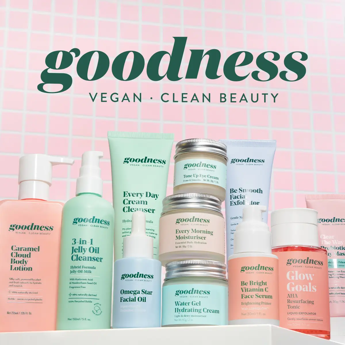 Goodness Products logo with various Goodness skincare products including lotion, cleansers, facial oil, eye cream, and moisturizers grouped together and displayed against a pink tiled background.