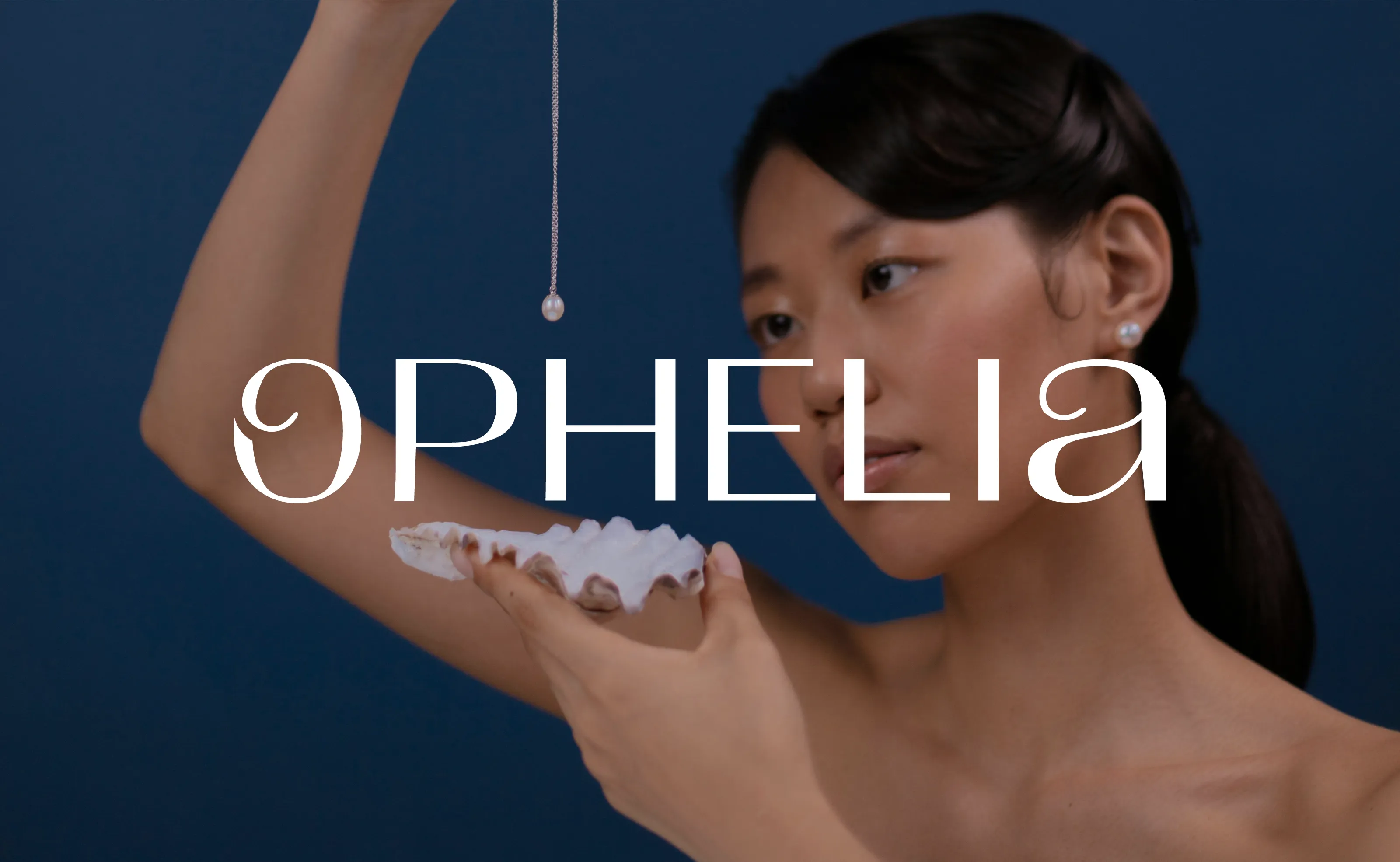 Editorial brand photography for Ophelia luxury jewellery, featuring a modern serif logo overlaid on an image of a model holding a pearl necklace and a seashell against a deep blue background.