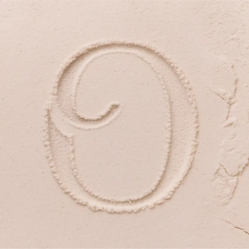 Modern jewelry brand logo design for Ophelia, featuring the stylized 'O' brand mark etched into a soft, sand-like texture to represent the Natural Perfection brand concept.
