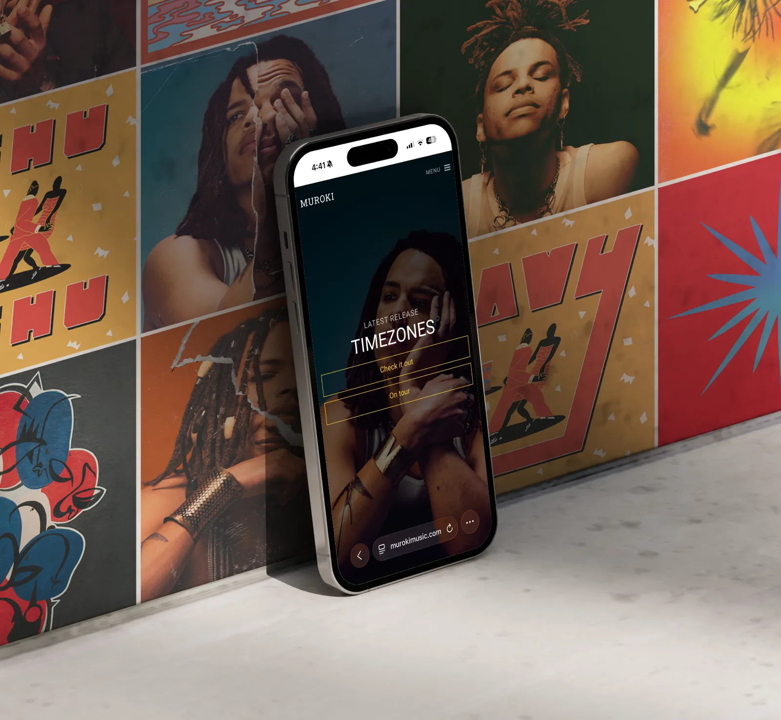 Smartphone leaning against a colorful wall with album art, displaying a responsive website design featuring artist Muroki and his latest release titled Timezones on the homepage.