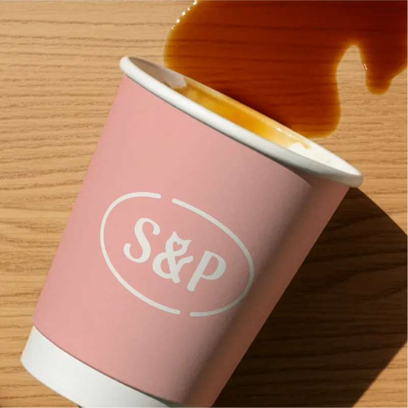 Custom branded coffee cup design for Sip & Purr, showing the pink secondary logo on a paper takeaway coffee cup spilled on a wooden table.