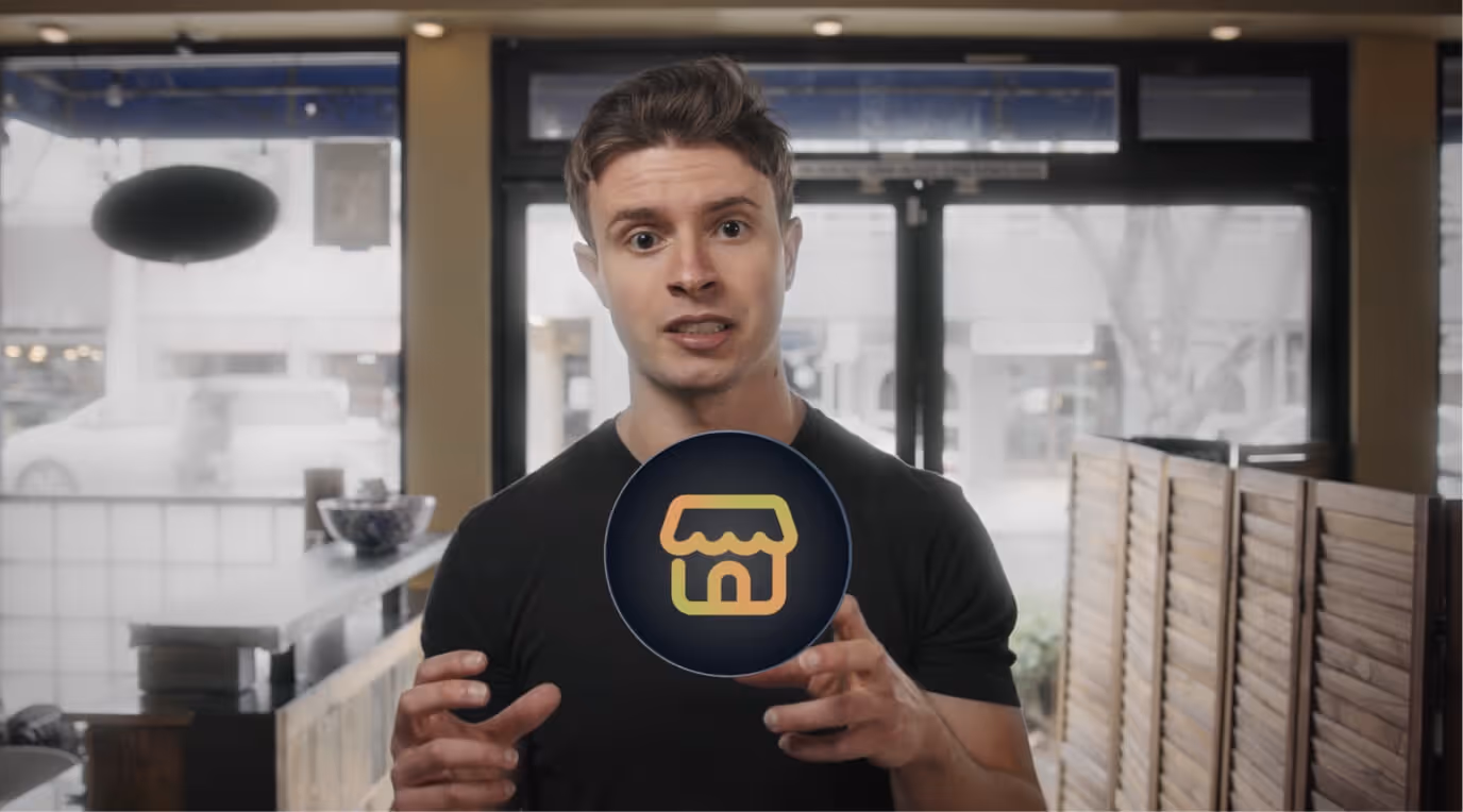 Young man in a black shirt standing indoors with a glowing small store icon between his hands.