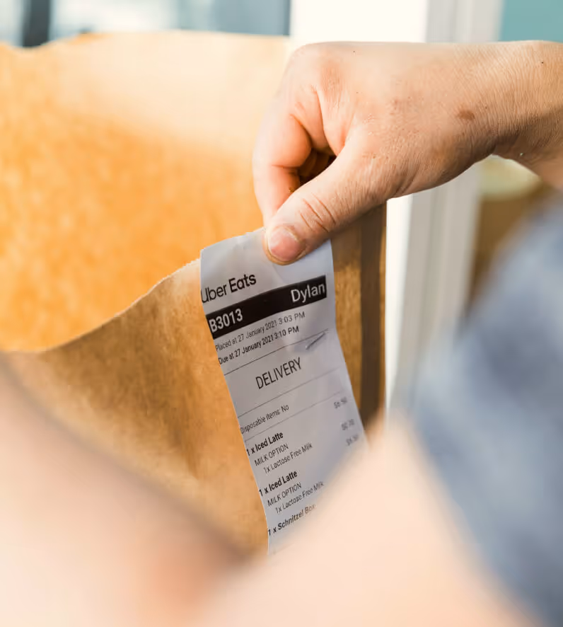 Hand holding an Uber Eats receipt attached to a brown paper delivery bag.