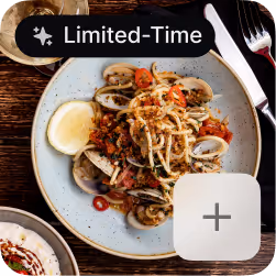 Plate of spaghetti with clams, cherry tomatoes, herbs, and a lemon wedge on a wooden table.