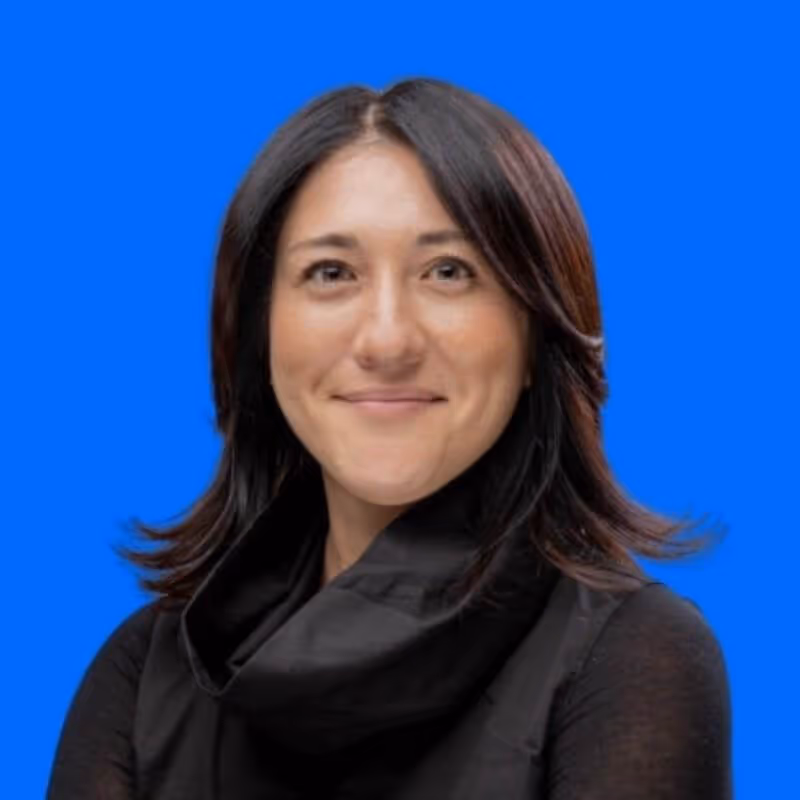 Smiling woman with shoulder-length dark hair wearing a black scarf and top against a blue background.