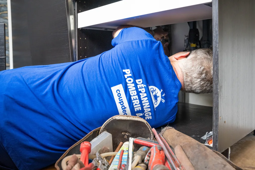 plombier t-shit bleu sous un évier de cuisine pour réparer les tuyaux d'évacuation et outils devant le meuble