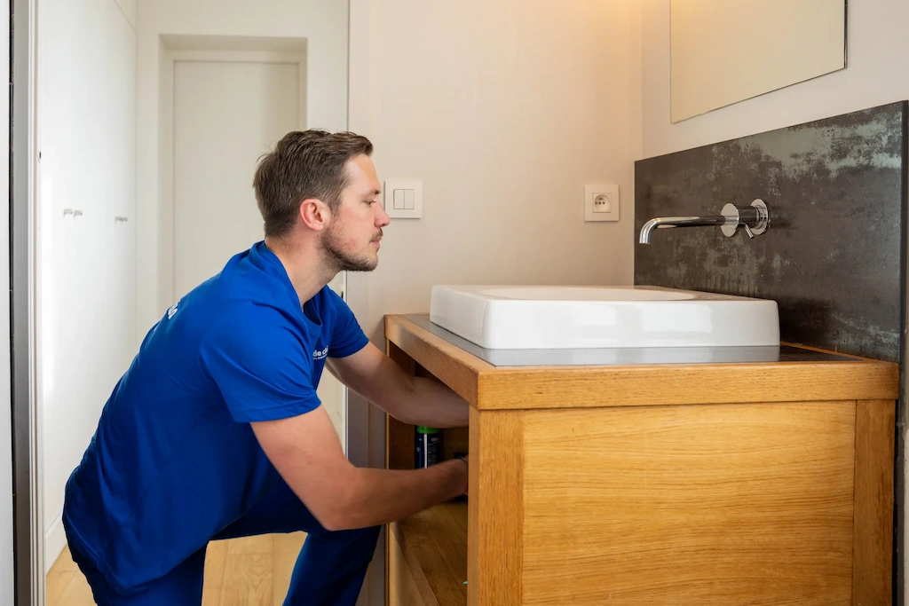 Robinet d’évier qui fuit par le dessous avec des gouttes d’eau visibles sous la base du mitigeur, illustrant une fuite de plomberie sous l’évier due à un joint usé ou un raccord desserré.