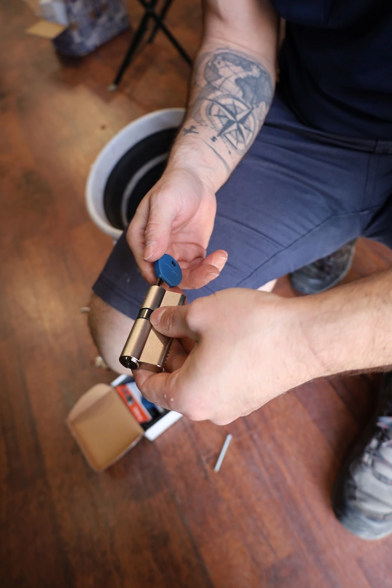 Personne tenant un cylindre de serrure en laiton et une clé bleue.