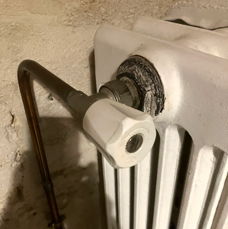 Gros plan sur une vanne de radiateur blanc avec une canalisation en cuivre fixée à un mur texturé beige.