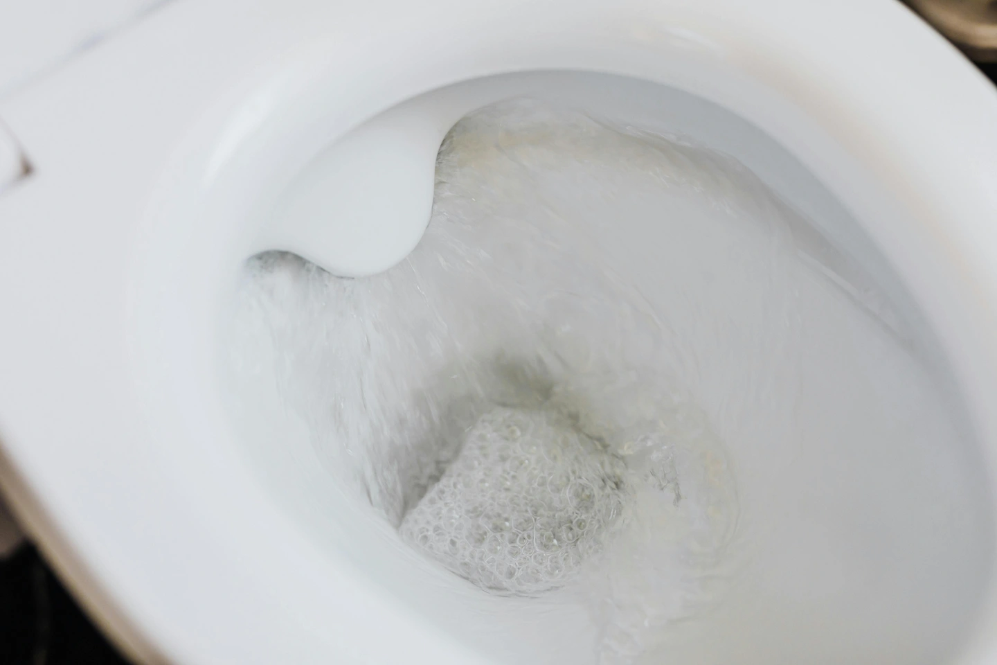 Vue rapprochée d'une chasse d'eau de toilettes en train de couler avec de l'eau et des bulles dans la cuvette blanche.