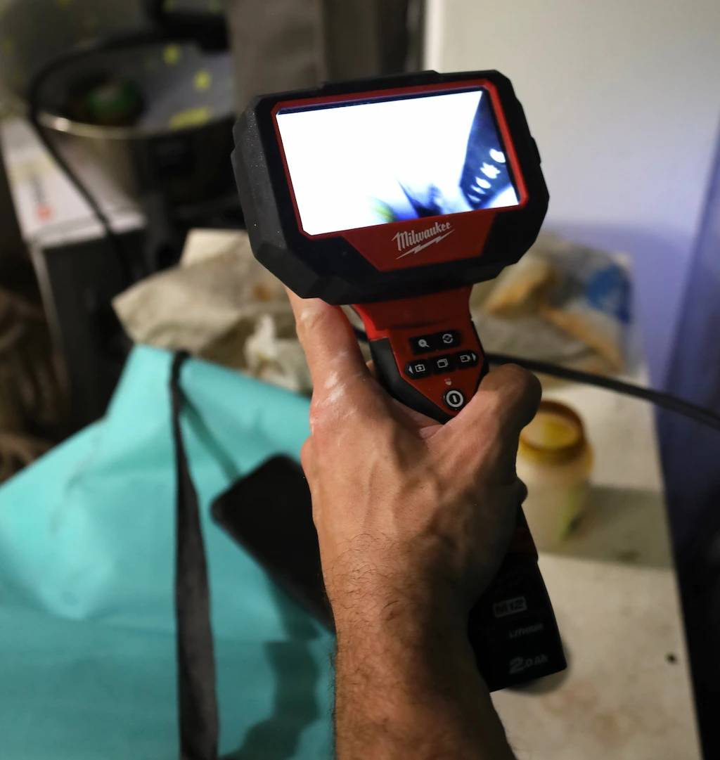 Main tenant un endoscope numérique Milwaukee avec écran affichant une image floue, utilisé pour inspecter des canalisations.
