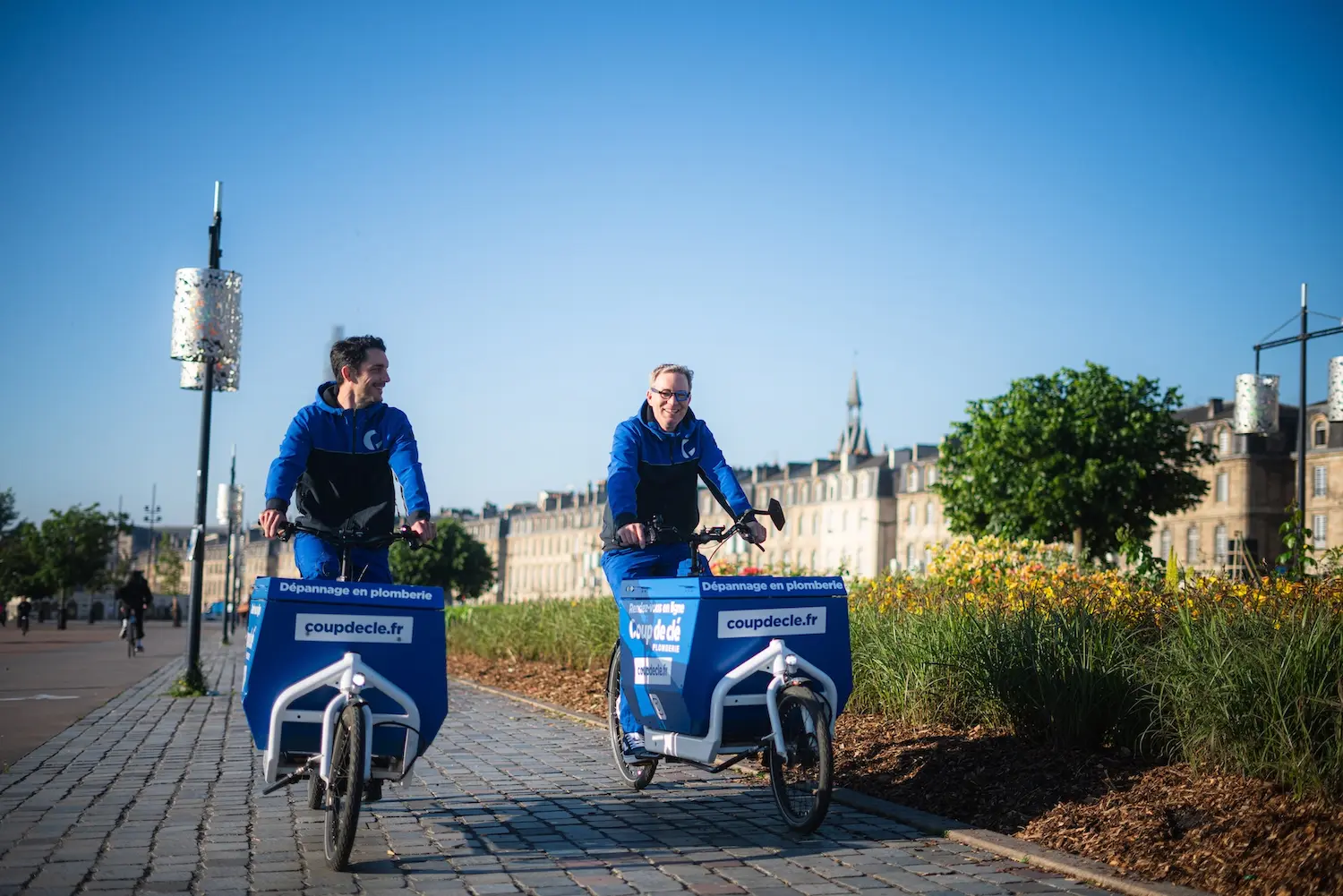 Deux techniciens souriants roulant à vélo cargo en ville