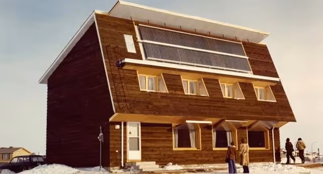 Wooden 1970's house with snow and people outside.