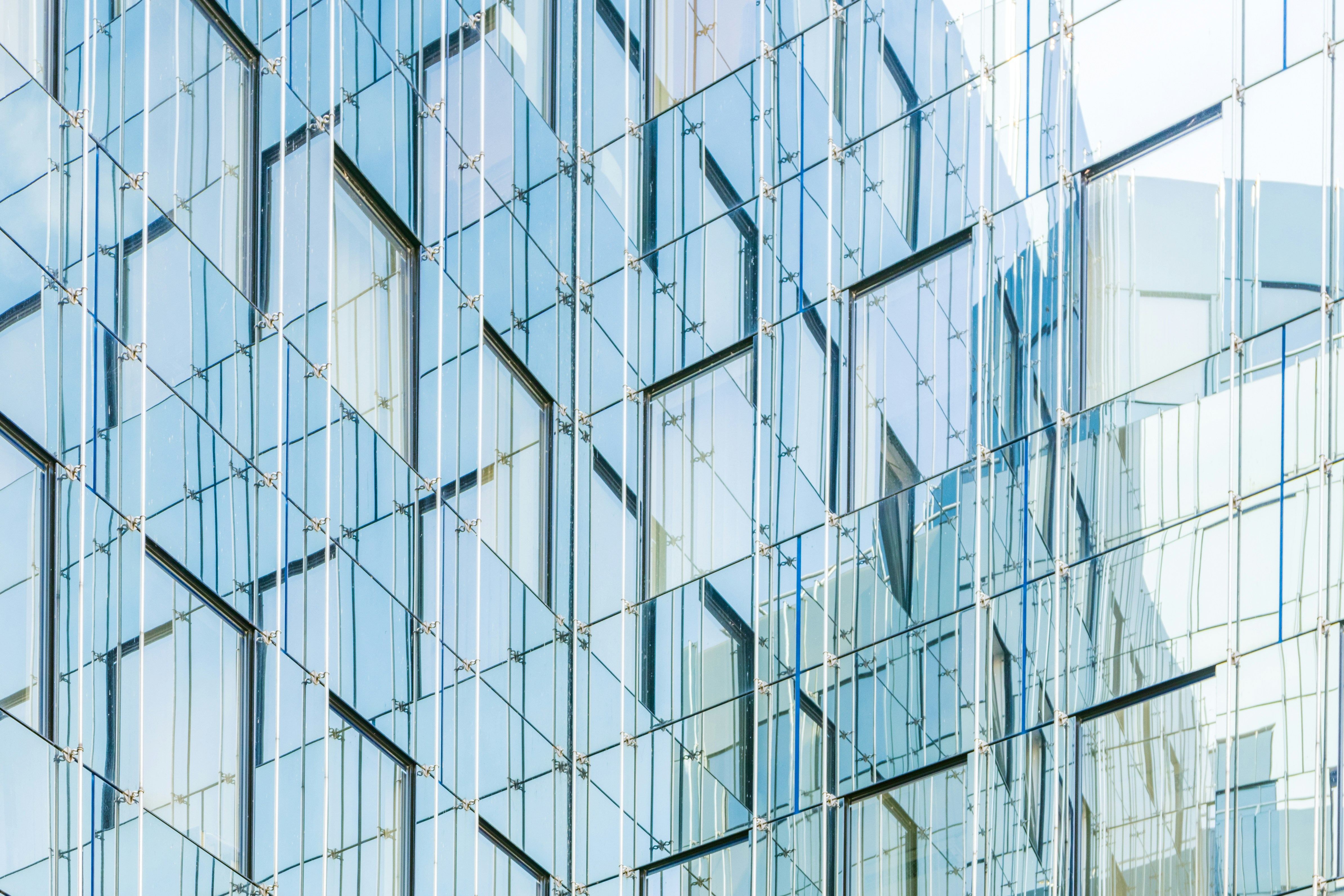 Close-up view of a modern glass building facade with repeating geometric window panels reflecting the sky and surrounding structures.