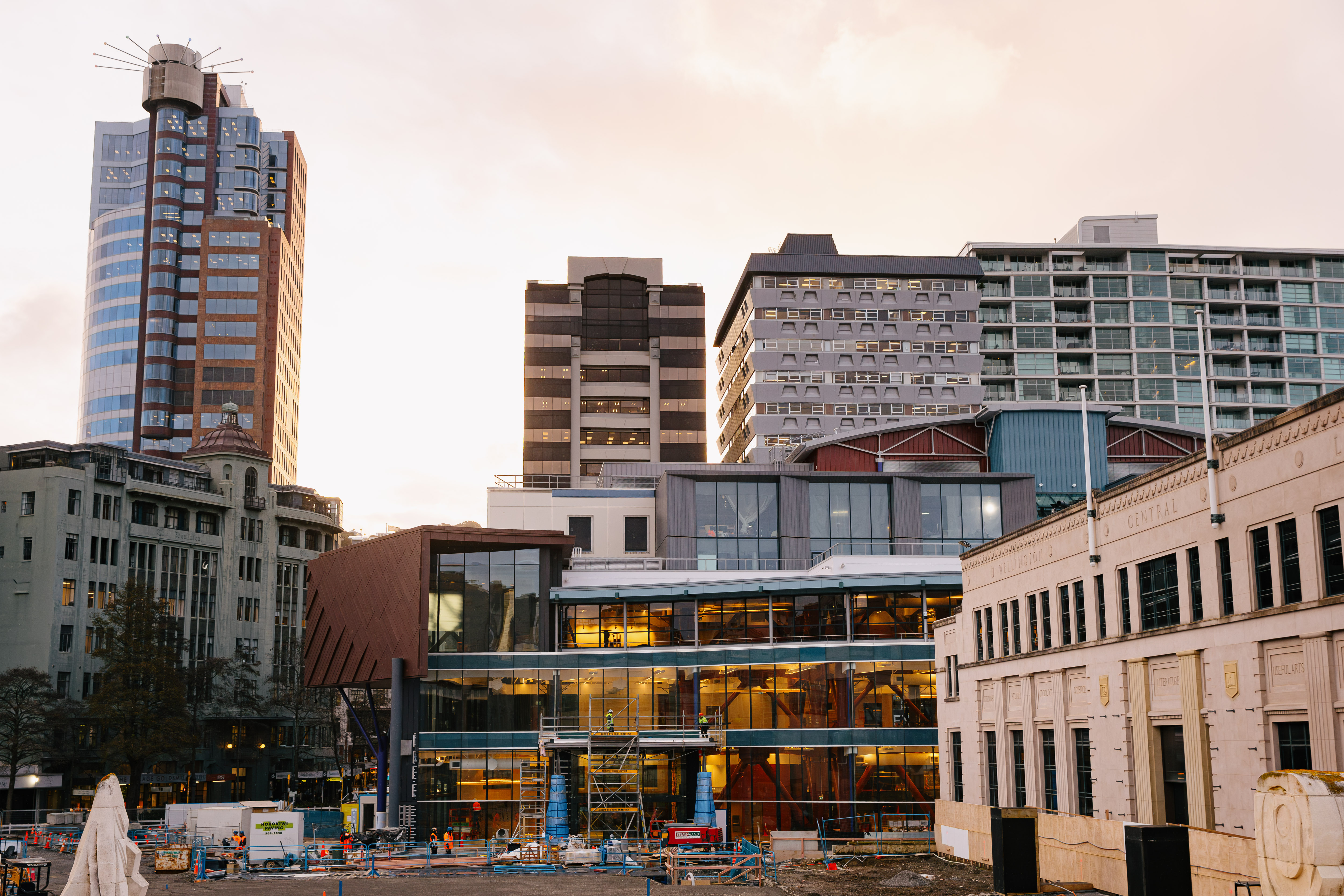 A wide-angle view of a contemporary building with detail showing a glass façade framed by diagonal metal fins and copper-toned cladding in one section and teal linear cladding in another.