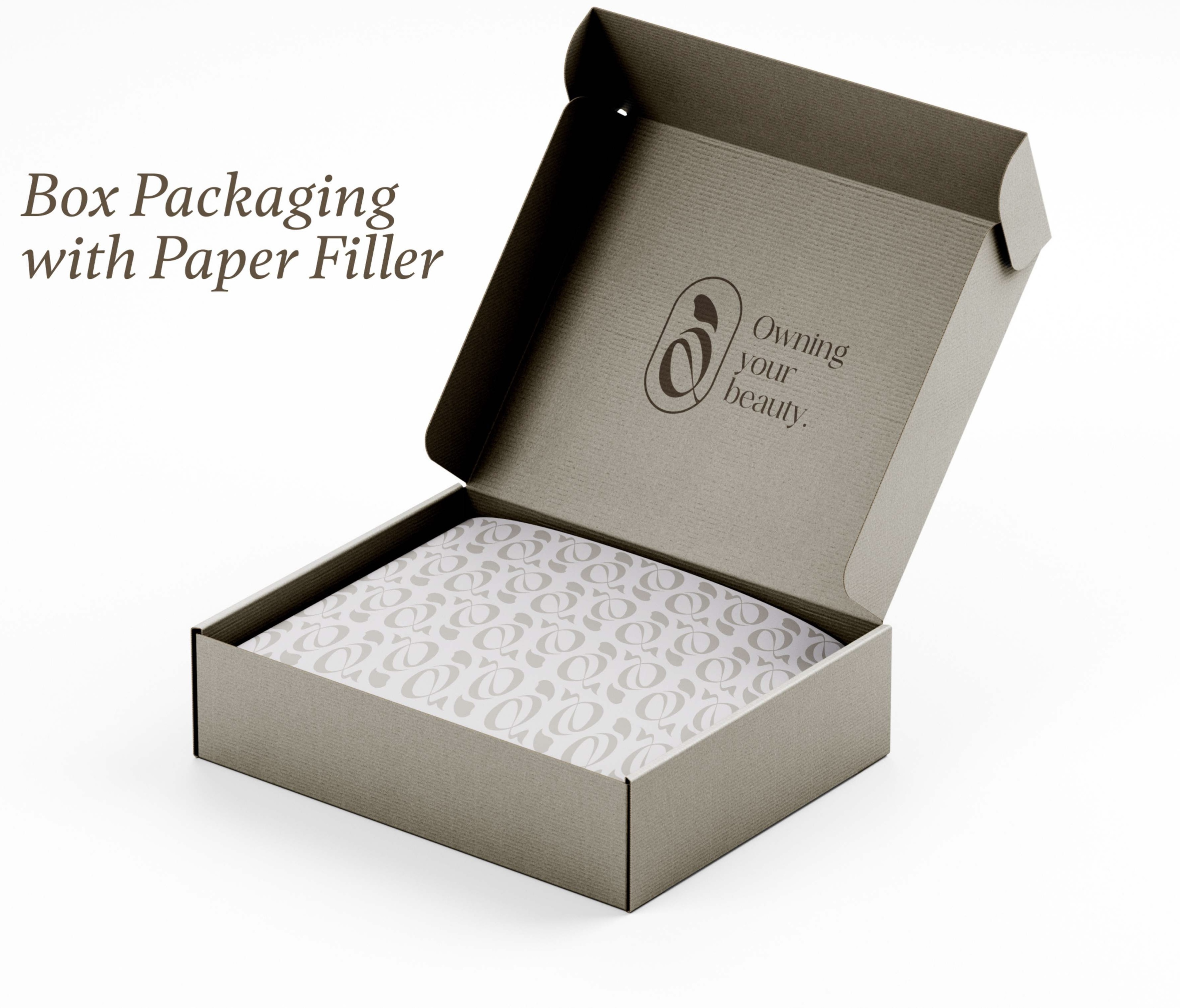 Open cardboard box with branded paper filler inside and the text 'Owning your beauty.' printed on the box lid.