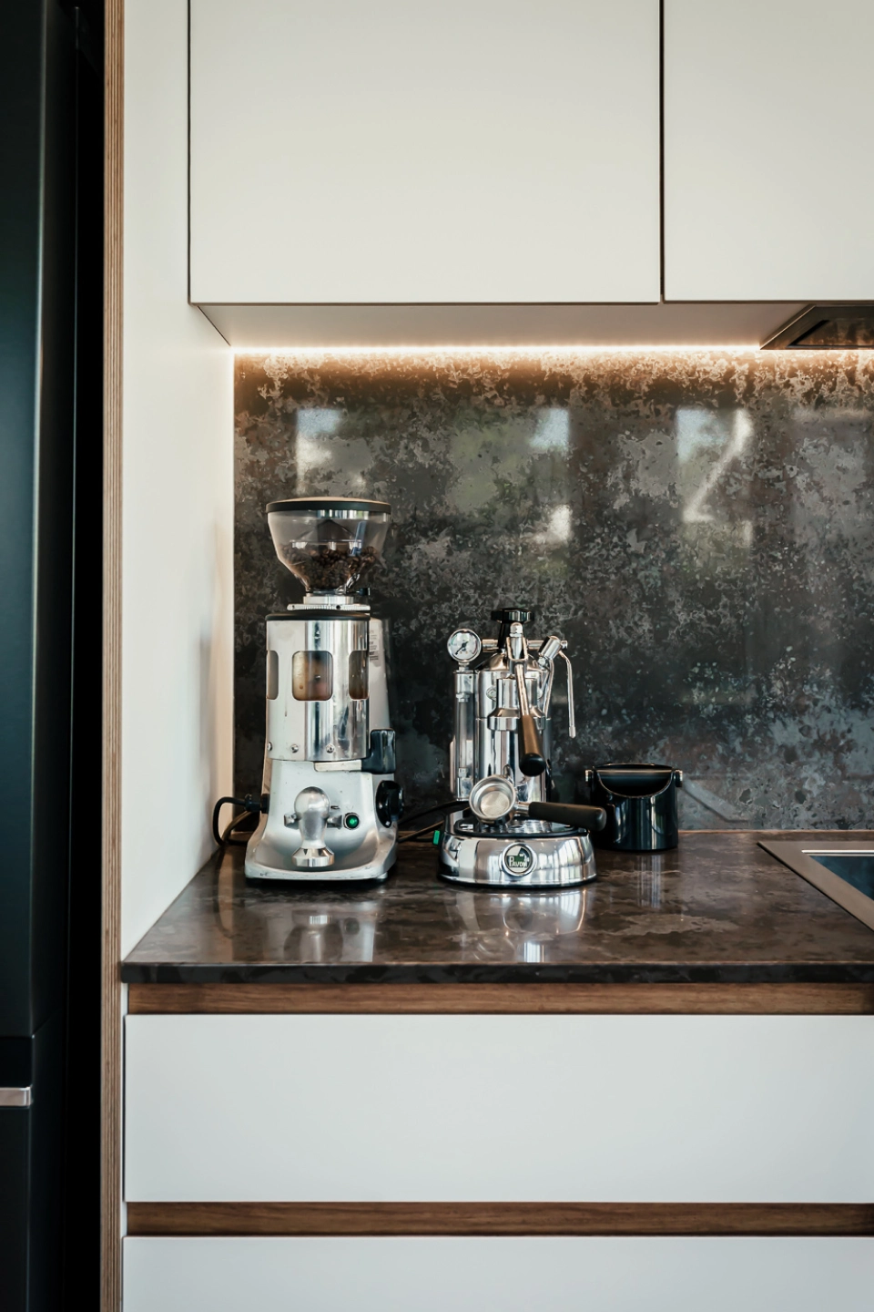 A coffee machine and grinder on a dark kitchen bench.