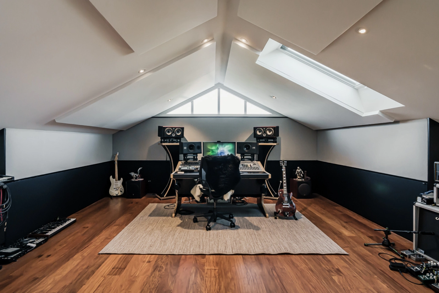 A home recording studio features a 
desk chair, extensive recording equipment, and musical instruments.
