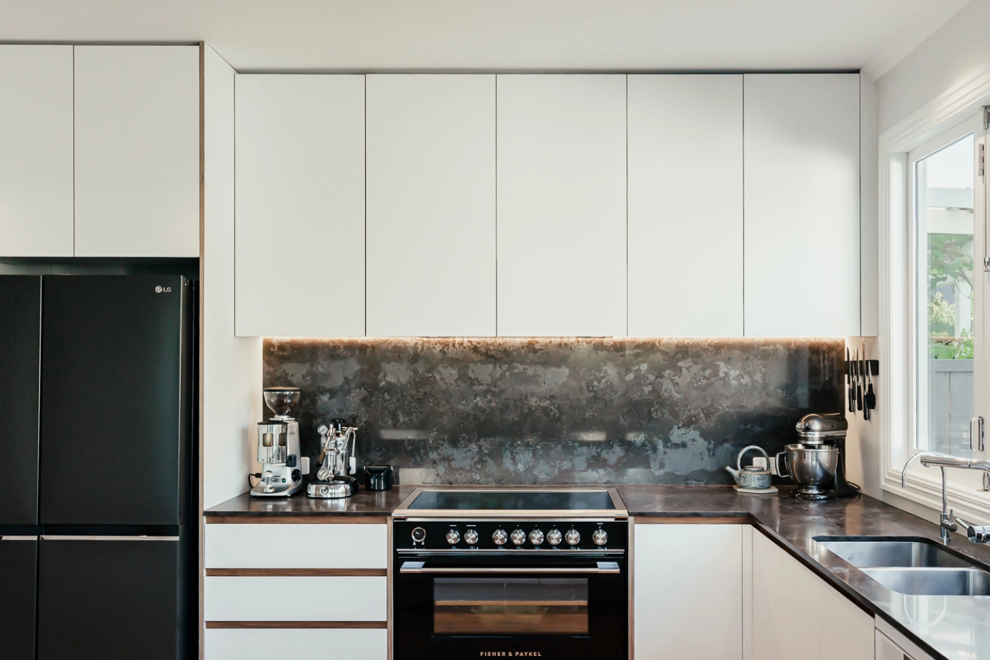 A modern kitchen with white cabinets, a dark backsplash, and black appliances.
