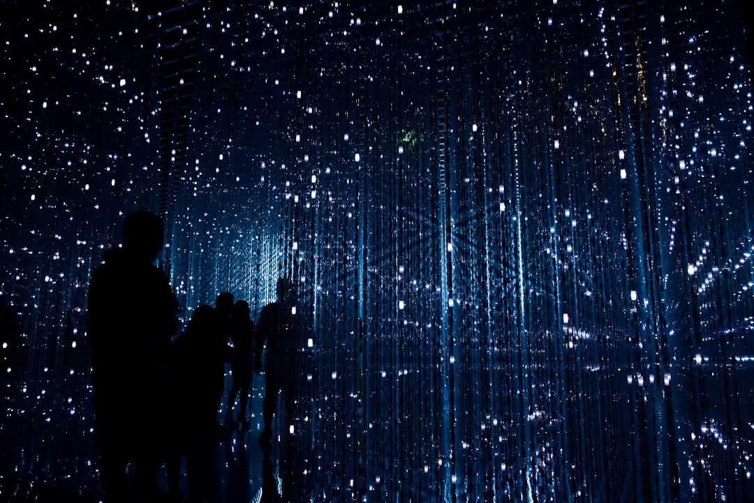 Des silhouettes se découpent devant une installation artistique numérique composée de lumières bleues en cascade, symbolisant l’avenir des tendances en matière d’IA générative.