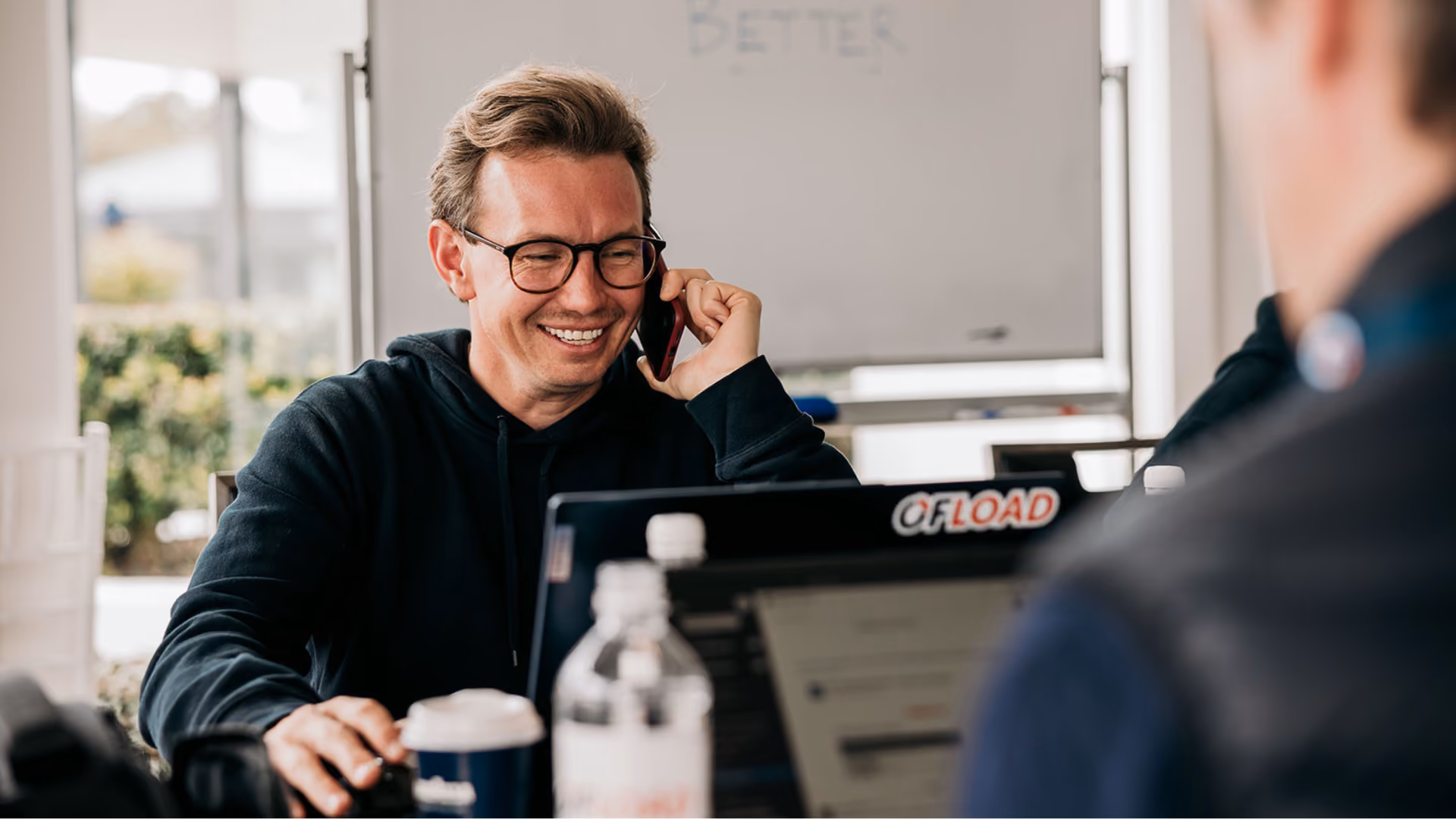 Small business owner smiling while talking to someone on the phone, while looking at his work laptop